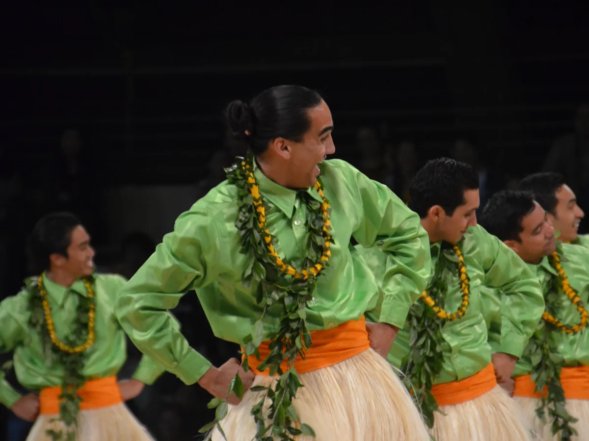 Male hula dancers in green shirts and ti-leaf lei performing on stage